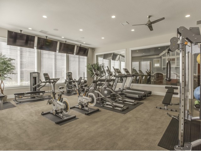 Fitness center with 2 treadmills, 2 ellipticals, quad machine, hamstring machines, free weights, exercise balls and bands, and four televisions