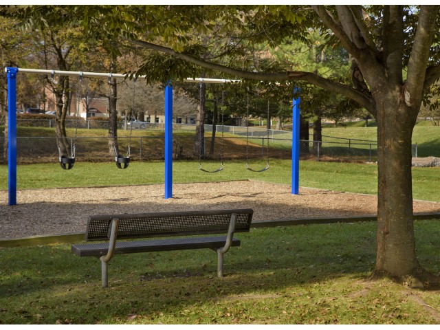 Playground and bench in wooded area at Piney Ridge Apartments & Townhomes.