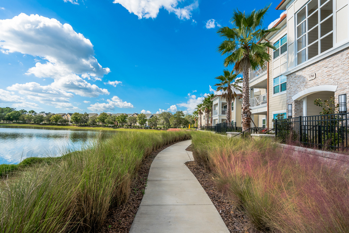 View of Walking Trail, Showing Walking Path, Lake to the Left, and Building Exterior to the Right at The Marq Highland Park Apartments