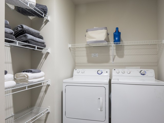 View of Laundry Room, Showing Side By Side Washer and Dryer and Towels at Cottonwood Westside Apartments