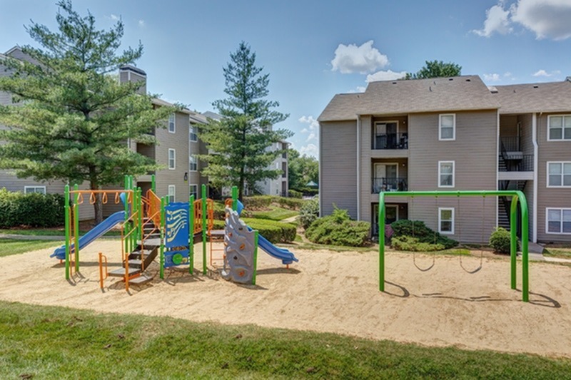 View of Playground, Showing Equipment, Swings, Slides, and Apartment Buildings in Background at 1070 Main Apartments