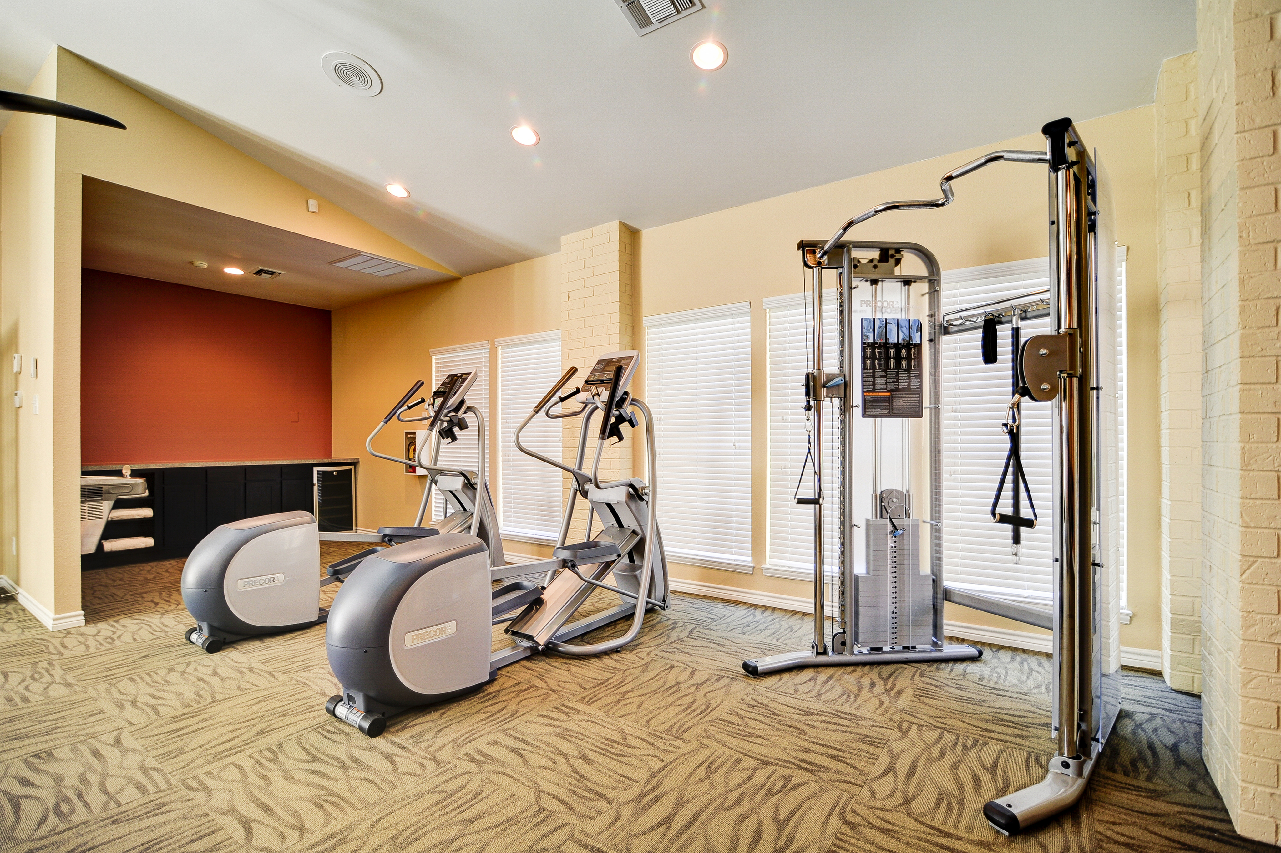 View of Fitness Center, Showing Ellipticals, Water Fountain, and Cable Machine at The Oaks of North Dallas Apartments
