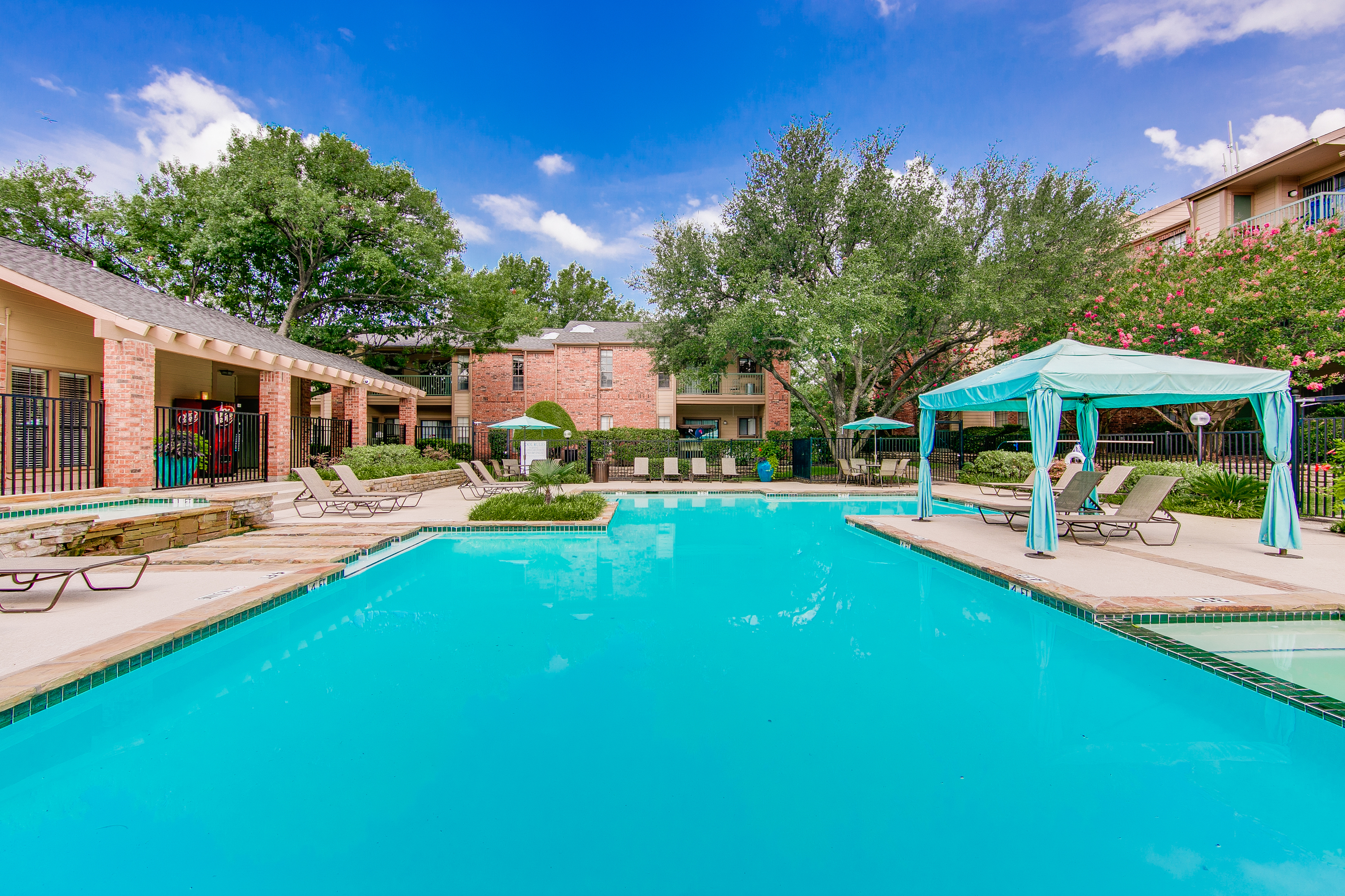 View of Pool, Showing Fenced-In Area, Loungers, Picnic Area, and Cabanas at The Oaks of North Dallas Apartments