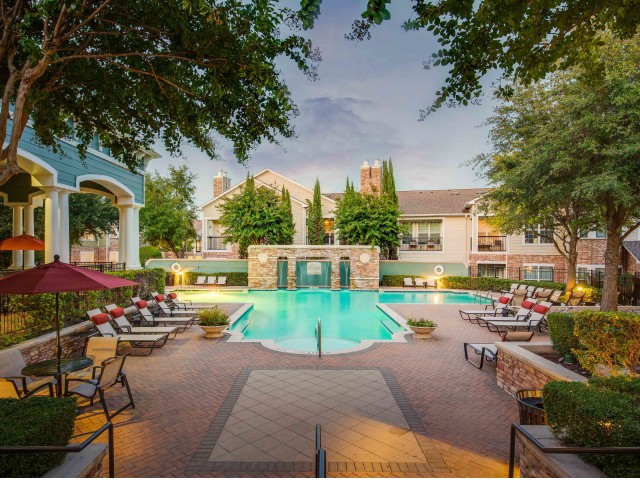 View of Pool Area, Showing Loungers, Tables with Umbrellas, Chairs, and Landscaping at Cottonwood Ridgeview Apartments