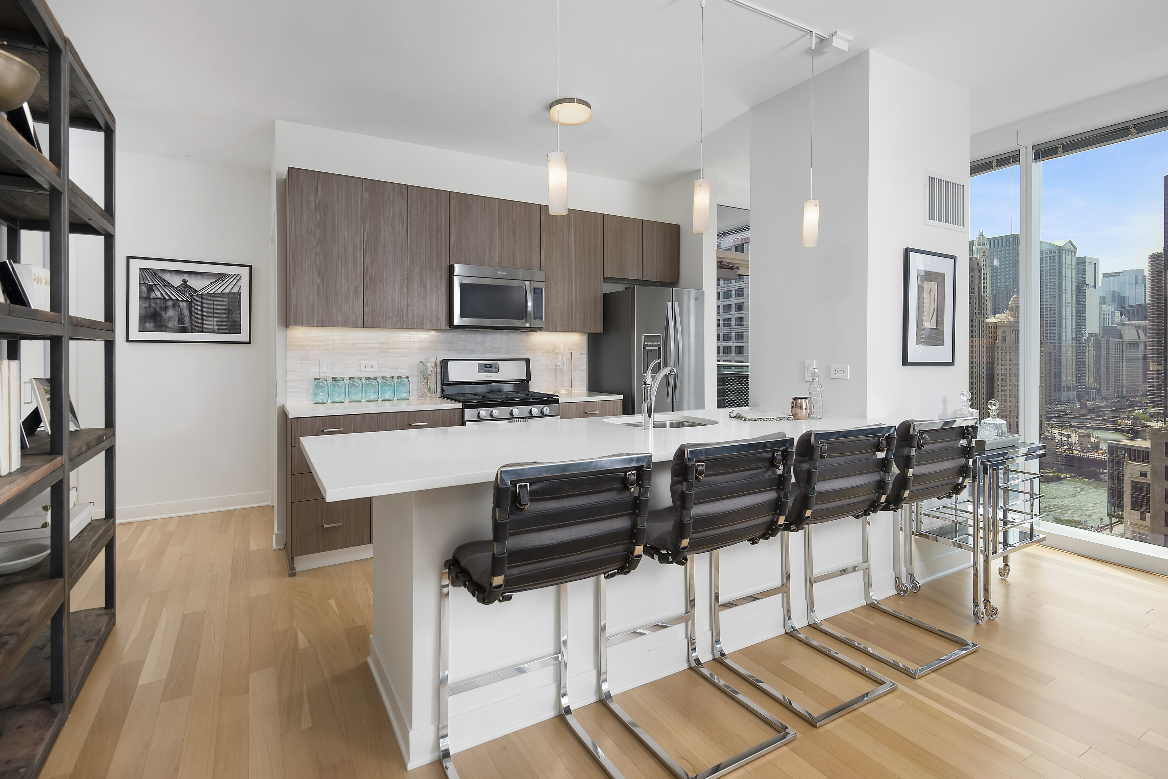 Model kitchen with stainless steel appliances, an island, quartzite stone countertops, wood flooring, and floor-to-ceiling windows with a city view