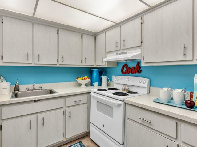 the dunes Indian harbour beach florida furnished kitchen with light cabinetry with modern pulls, wood-plank floors, white appliances, and abundant overhead lighting
