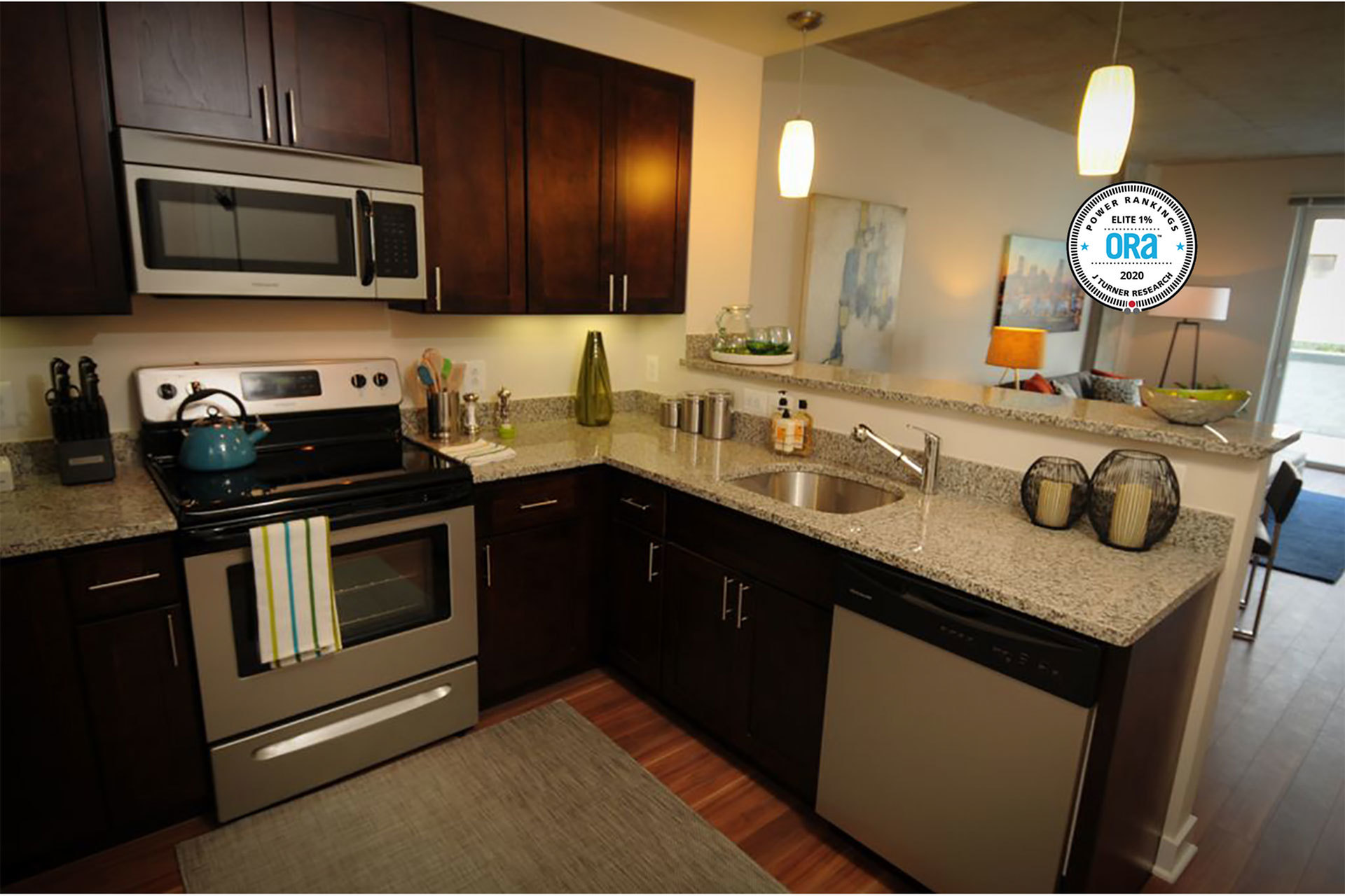 Kitchen with stainless steal appliances, granite counters, and a breakfast bar over looking the living space. ORA 2020 Power Rankings J Turner Research seal superimposed in the right corner of the photo.